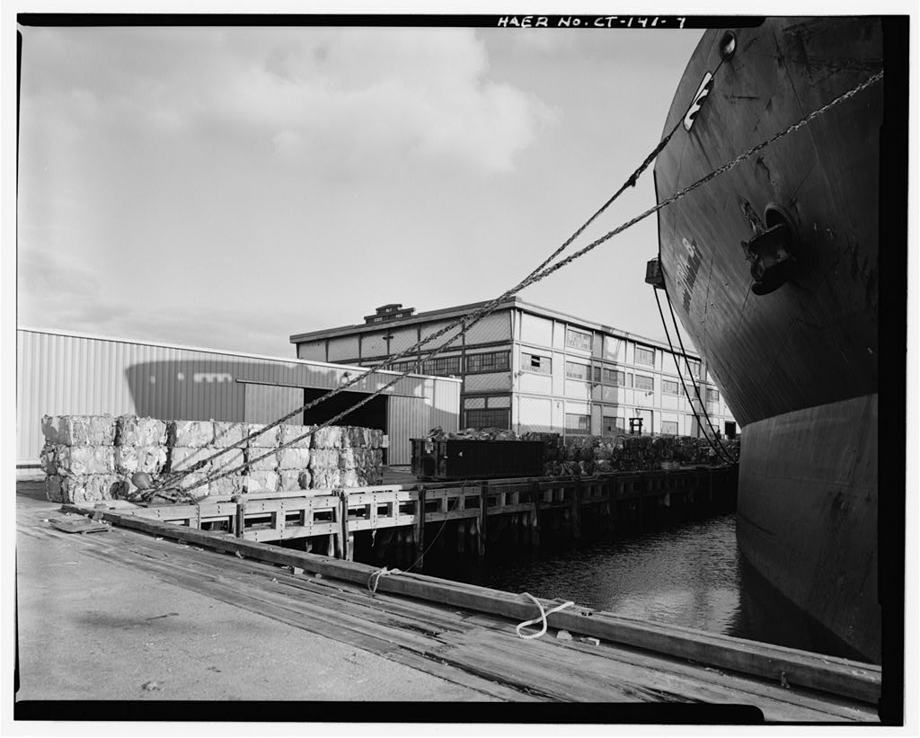 View southeast, showing west side from land, with waste paper bundled on dock, awaiting loading onto Odigitria B